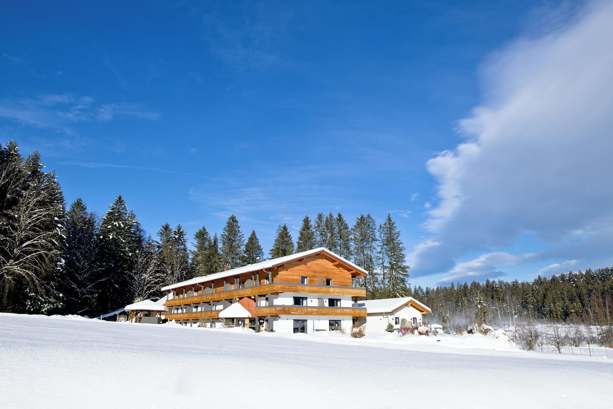 A multi-story wooden lodge with balconies, surrounded by snow-covered trees and a clear sky.
