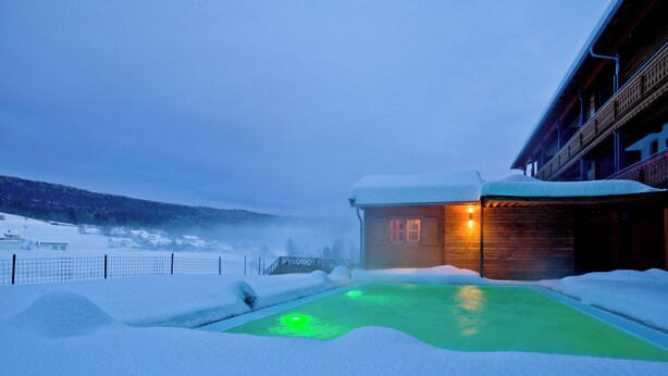 Une cabane en bois avec une piscine chauffée, entourée de neige.