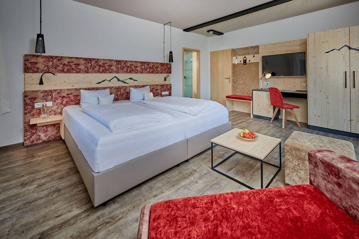 A modern bedroom with a large bed, a desk, a TV, and a red chair.