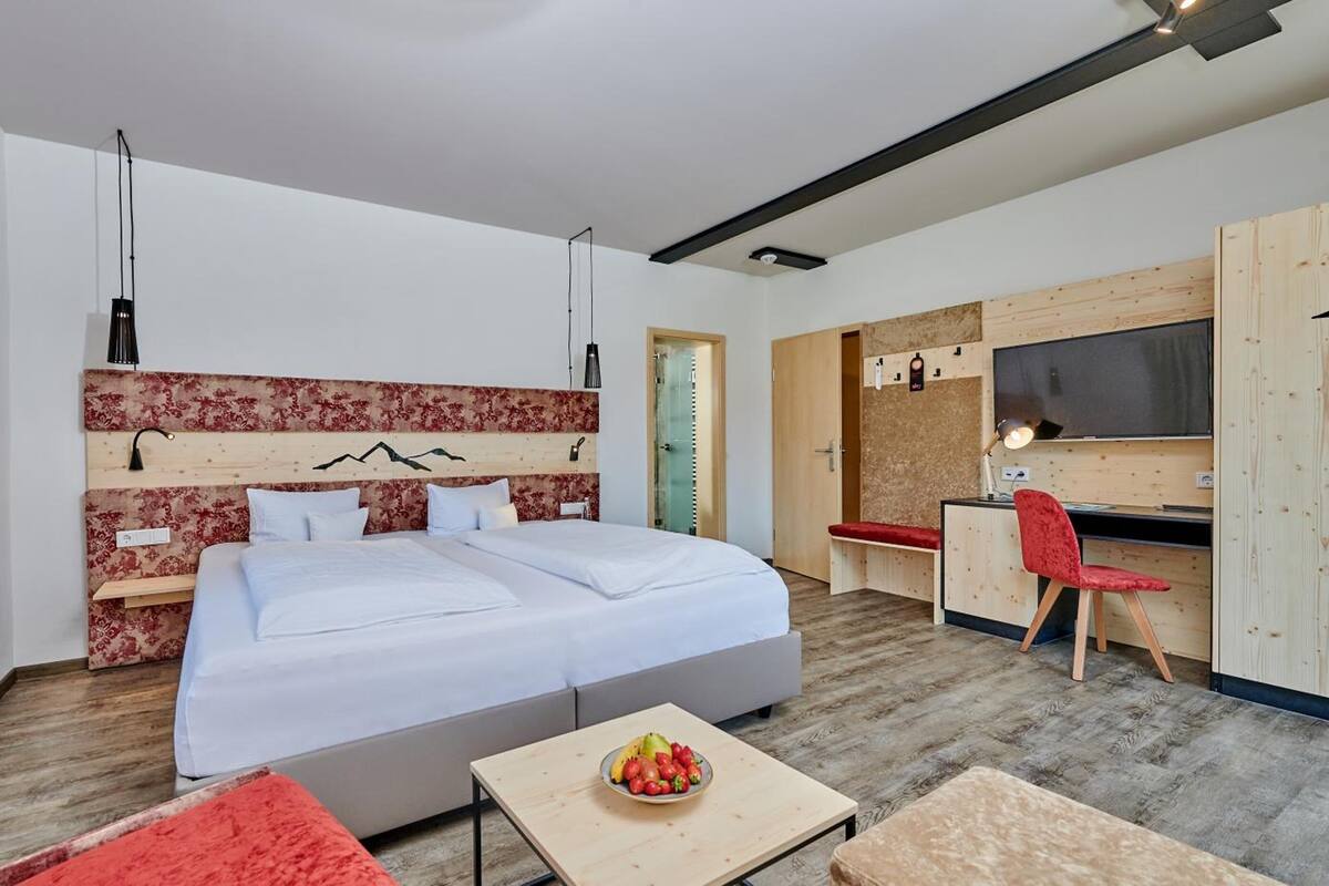 A modern hotel room with a large bed, a desk, a TV, and a small table with fruit.