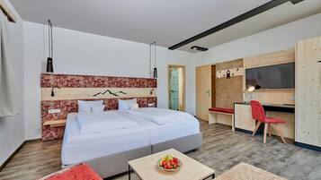 A modern hotel room with a large bed, a desk, a TV, and a small table with fruit.