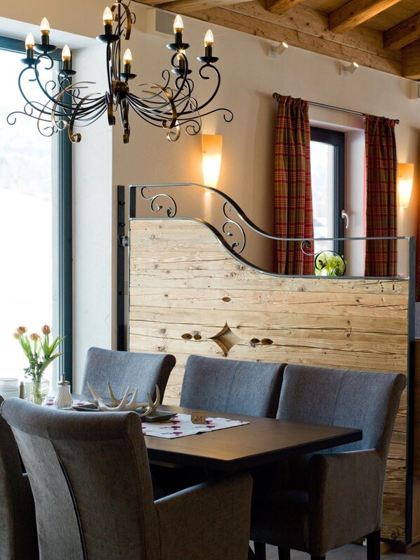 A dining area with a wooden headboard, a chandelier, and plaid curtains. - Hotel Moorhof (Neuschoenau)