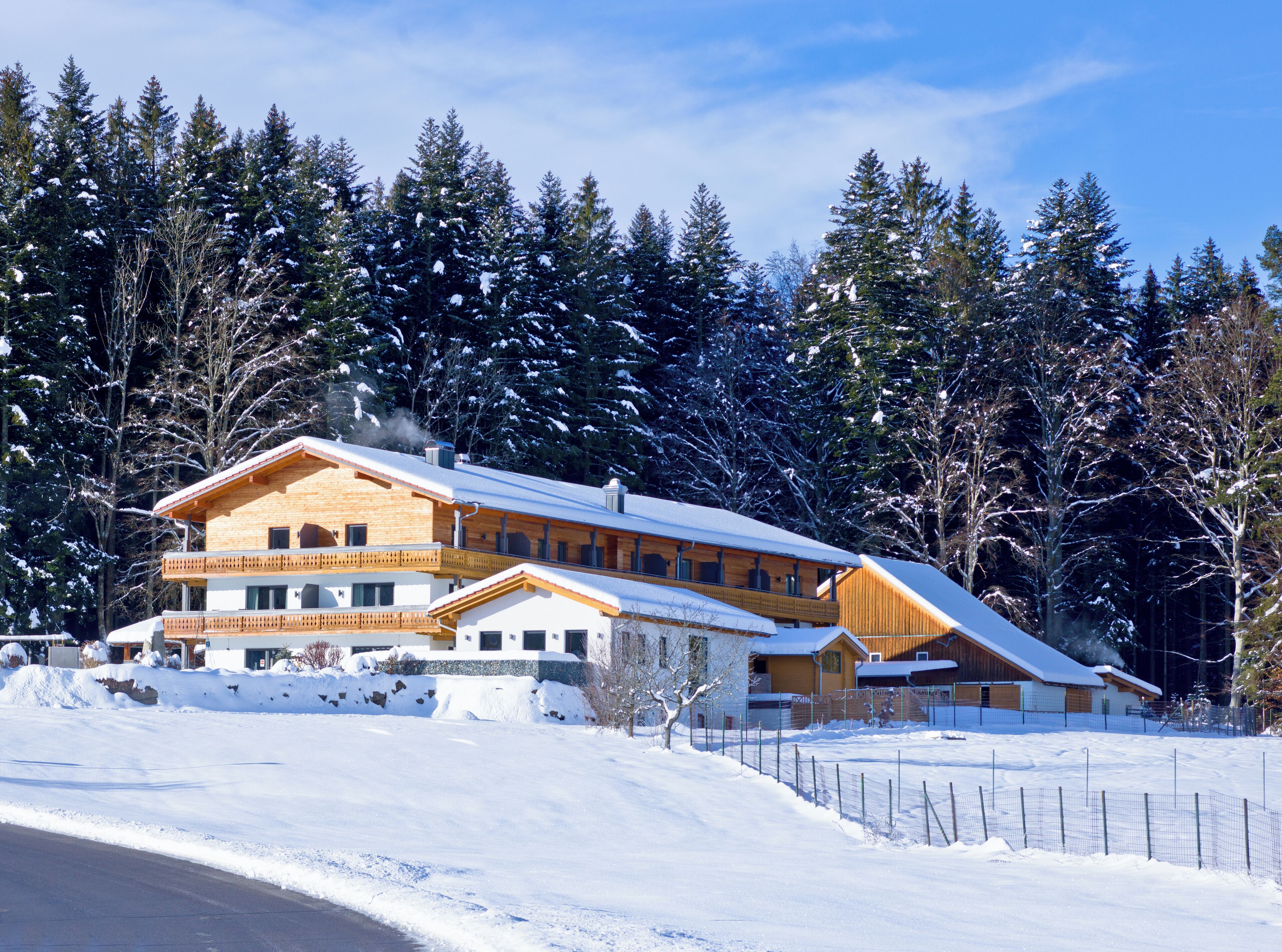 A large wooden chalet with multiple balconies and a snow-covered roof, surrounded by dense forest.