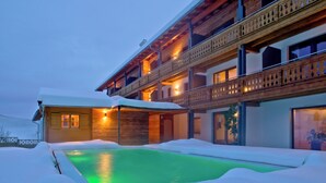 Un bâtiment enneigé doté d’une piscine, de balcons en bois et d’une lumière intérieure chaleureuse.