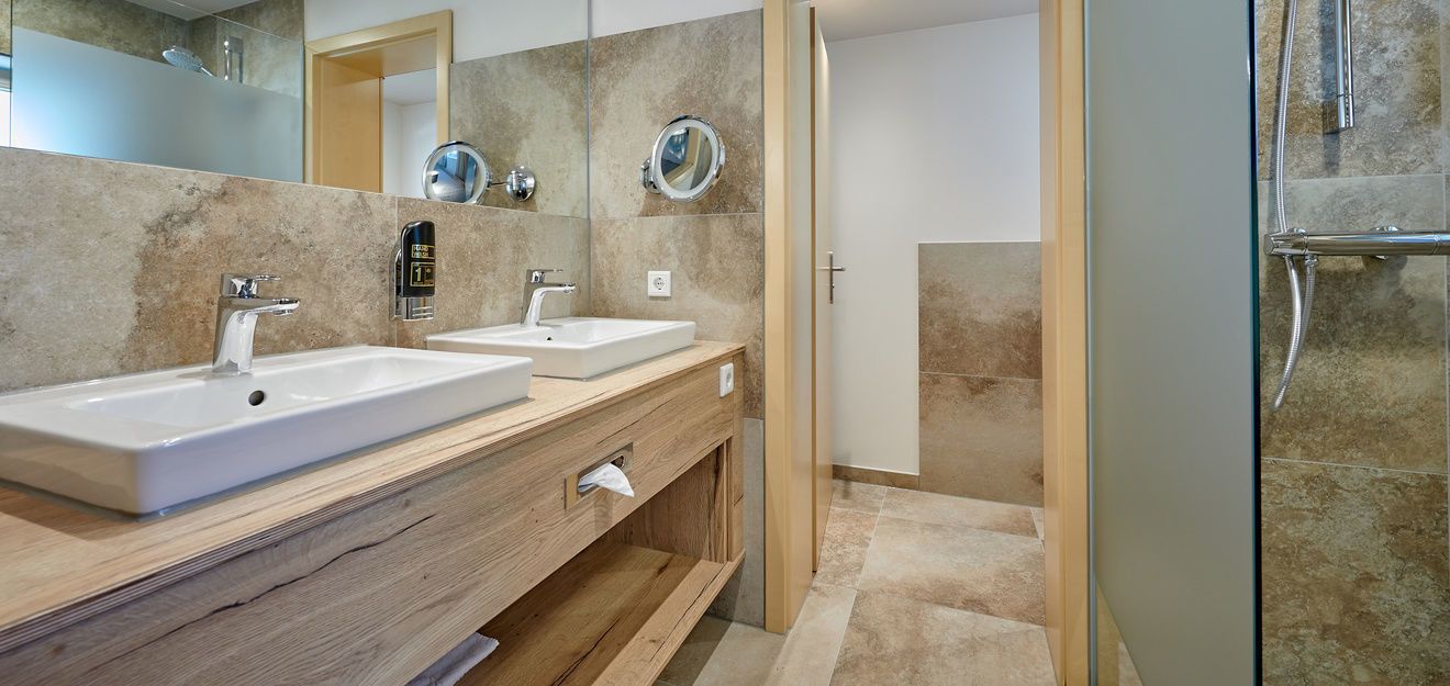 A modern bathroom with two sinks, a mirror, and a shower area.