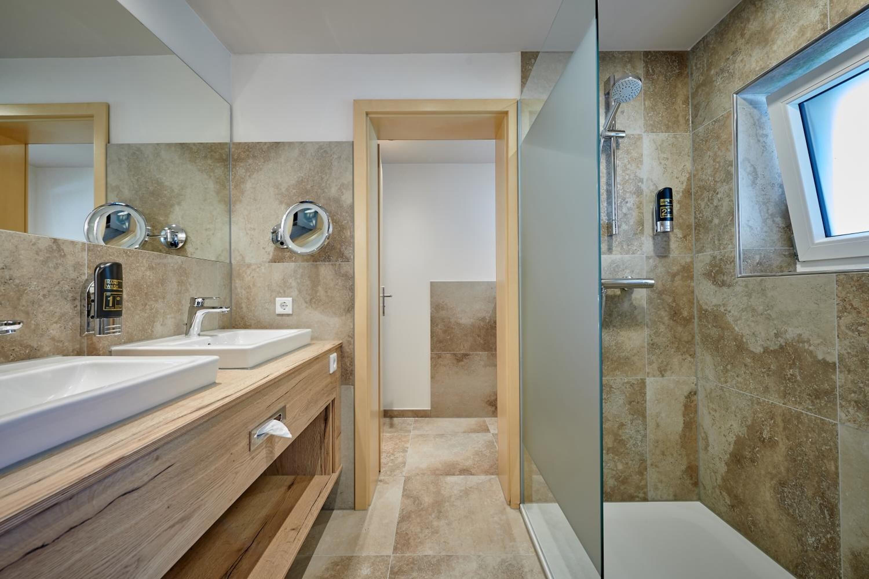 A modern bathroom with two sinks, a shower, and a large mirror.