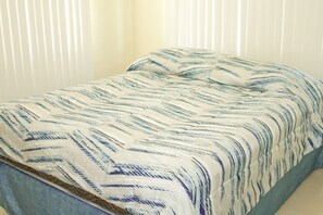 Ein Bett mit einem gemusterten Überwurf in einem Raum mit vertikalen Jalousien.