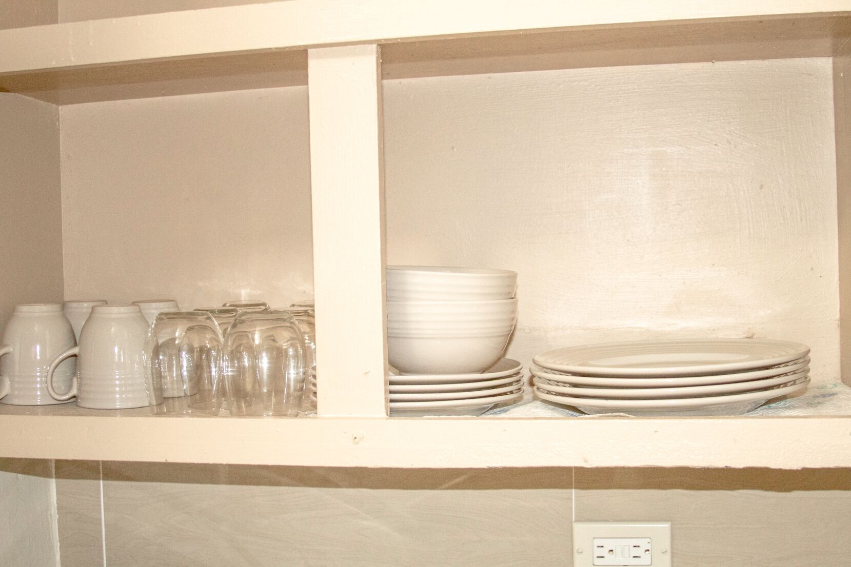 Une étagère de cuisine avec des tasses blanches, des verres et des assiettes empilées.