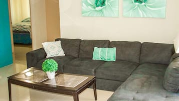 Un salon avec un canapé gris foncé, deux coussins décoratifs, une petite plante en pot et deux tableaux représentant des motifs floraux, accrochés au mur.