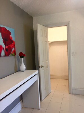 Enter a serene space with a white door leading to a cozy room, featuring a stylish desk with a vase and a beautiful painting of red roses.