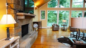 Une pièce spacieuse avec une cheminée en pierre, de grandes fenêtres et un plancher en bois.