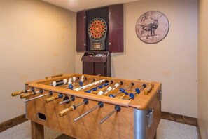 A foosball table in a room with a dartboard and a clock on the wall.