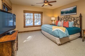 Ein Schlafzimmer mit Bett, Fernseher, Fenster und Deckenventilator.