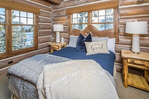 Une chambre à coucher située dans un chalet en rondins, avec un grand lit, deux tables de chevet et une vue sur des arbres couverts de neige.