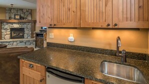 A kitchen with wooden cabinets, a stone fireplace, a granite countertop, and a stainless steel sink. - Luxury 5 Bedroom Big Sky Retreat (Big Sky)