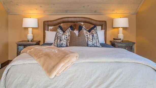 Un grand lit avec une tête de lit en bois, deux tables de chevet avec des lampes et des coussins décoratifs.