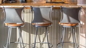 Three bar stools with metal legs and wooden seats, positioned in front of a kitchen counter with a checkered tile backsplash and coffee machines. - Luxury 5 Bedroom Big Sky Retreat (Big Sky)