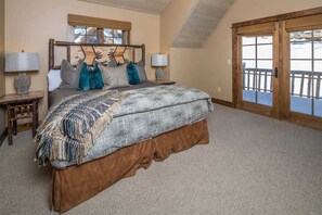 Ein Schlafzimmer mit einem großen Bett, zwei Nachttischen, einem Fenster mit Jalousien und Blick auf einen Balkon.