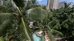 A rooftop pool surrounded by lush palm trees and greenery, with a view of tall buildings in the background. - 🌤Stay in our Breezy Bamboo Studio 🏘Now this is what we call home! 2QUEEN Beds (Honolulu)