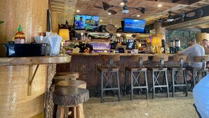 A rustic bar area with wooden stools, a bar counter, and a television mounted on the wall. - 🌤Stay in our Breezy Bamboo Studio 🏘Now this is what we call home! 2QUEEN Beds (Honolulu)