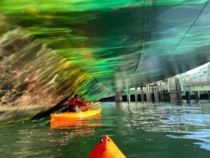 Une personne pratiquant le kayak sous un pont, l’eau ayant une teinte verdâtre.
