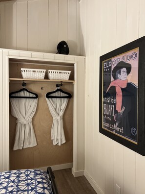 Une chambre avec un placard intégré, deux peignoirs blancs suspendus et une affiche accrochée au mur.