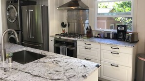 A kitchen with stainless steel appliances, a marble countertop, and a window with a view of greenery. - Eagle Harbor View Cottage (Bainbridge Island)