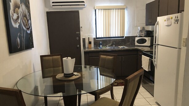 A modern kitchen with a glass dining table, dark wooden chairs, a white refrigerator, and a microwave. - PEDRO'S PLACE PRIVATE APARTMENT 2 BDRM 1 ba Free Power, Water and Internet (Sinajana)