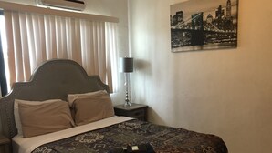 A hotel room with a bed, a nightstand, a lamp, and a cityscape painting on the wall. - PEDRO'S PLACE PRIVATE APARTMENT 2 BDRM 1 ba Free Power, Water and Internet (Sinajana)