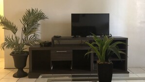A modern living room with a flat-screen TV on a black entertainment unit, two potted plants, and a tiled floor. - PEDRO'S PLACE PRIVATE APARTMENT 2 BDRM 1 ba Free Power, Water and Internet (Sinajana)