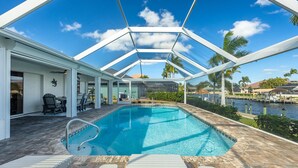 An outdoor swimming pool with a glass ceiling, surrounded by lounge chairs and a patio area. - Lovely waterfront gulf access, heated pool in SW Cape Coral awaits you. (Cape Coral)
