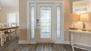 A white door with glass panels, a dining area with a wooden table and chairs, and a small table with a lamp and decorative items. - Lovely waterfront gulf access, heated pool in SW Cape Coral awaits you. (Cape Coral)
