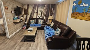 Een gezellige woonkamer met een bank, een bijzettafeltje en een bed met een decoratieve dekbedovertrek.
