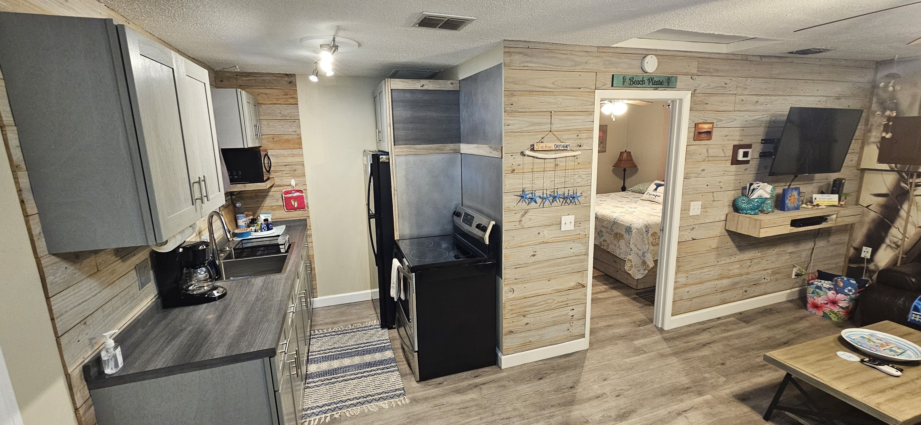 A compact room with a kitchenette, a bed, a TV, and a small seating area.