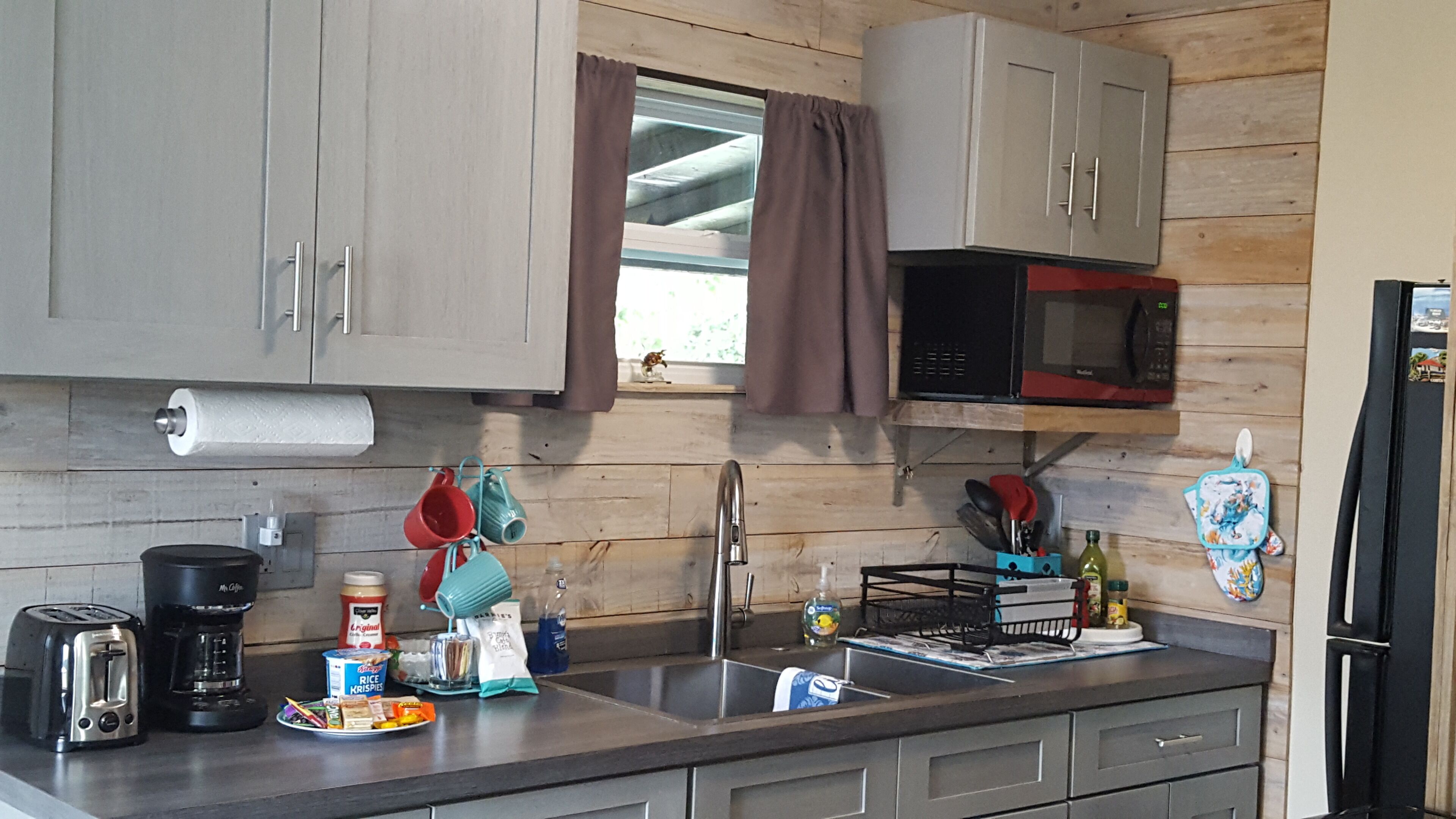 Una cocina con armarios de madera, un lavamanos de acero inoxidable, un microondas y varios utensilios de cocina sobre la encimera.
