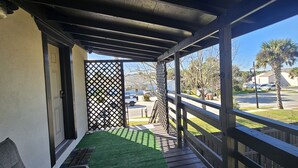 Een balkon met houten hekwerk, uitzicht op een straat met palmbomen, en een gebouw op de achtergrond.