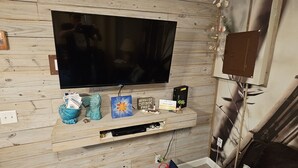Een flatscreen televisie bevestigd aan een houten wand, een klein plankje met decoratieve objecten, en een ingelijst schilderij.