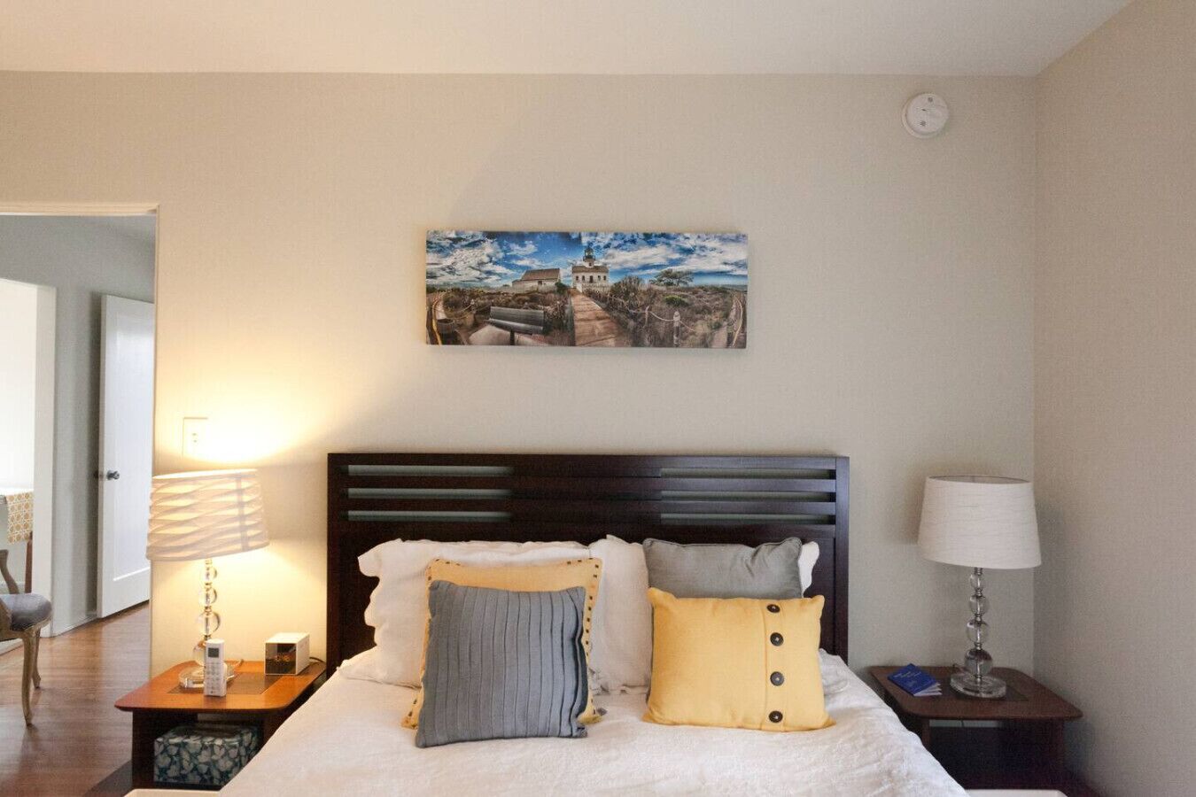 Ein Schlafzimmer mit einem Bett, zwei Nachttischen, einer Lampe, einem Bild an der Wand und einer Tür zu einem anderen Raum.