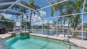 A swimming pool with a glass enclosure, surrounded by palm trees and a view of a body of water. -  Beautiful Southern Exposure,  with gorgeous sunsets on a waterway. (Marco Island)
