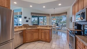 A kitchen with wooden cabinets, a stainless steel refrigerator, a built-in oven, and a large window providing a view of the outdoors. -  Beautiful Southern Exposure,  with gorgeous sunsets on a waterway. (Marco Island)