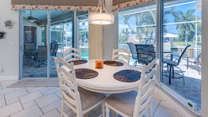 A dining area with a round table, white chairs, and a hanging light fixture. -  Beautiful Southern Exposure,  with gorgeous sunsets on a waterway. (Marco Island)
