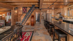 Ein Holzhütten-Interieur mit steinbelagtem Boden, Holzmöbeln, einer Bar und einer Treppe, die zu einer oberen Ebene führt.