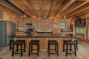 Cucina con pensili in legno, isola centrale con sgabelli e schienale in pietra.