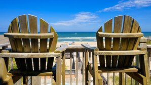 Twee houten Adirondack stoelen gericht op een strand met heldere lucht.