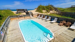 Een houten terras met een zwembad, ligstoelen en uitzicht op het strand.