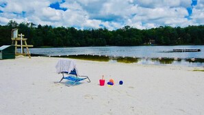 En strand med en trästol, en hink och en boll i sanden, nära en sjö.
