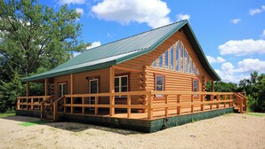 Eine Blockhütte mit grüner Dachdeckung, einer Holzdachterrasse und einer Veranda mit Stufen.
