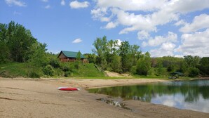 Eine Blockhütte am See mit Sandstrand und einer kleinen Anlegestelle.