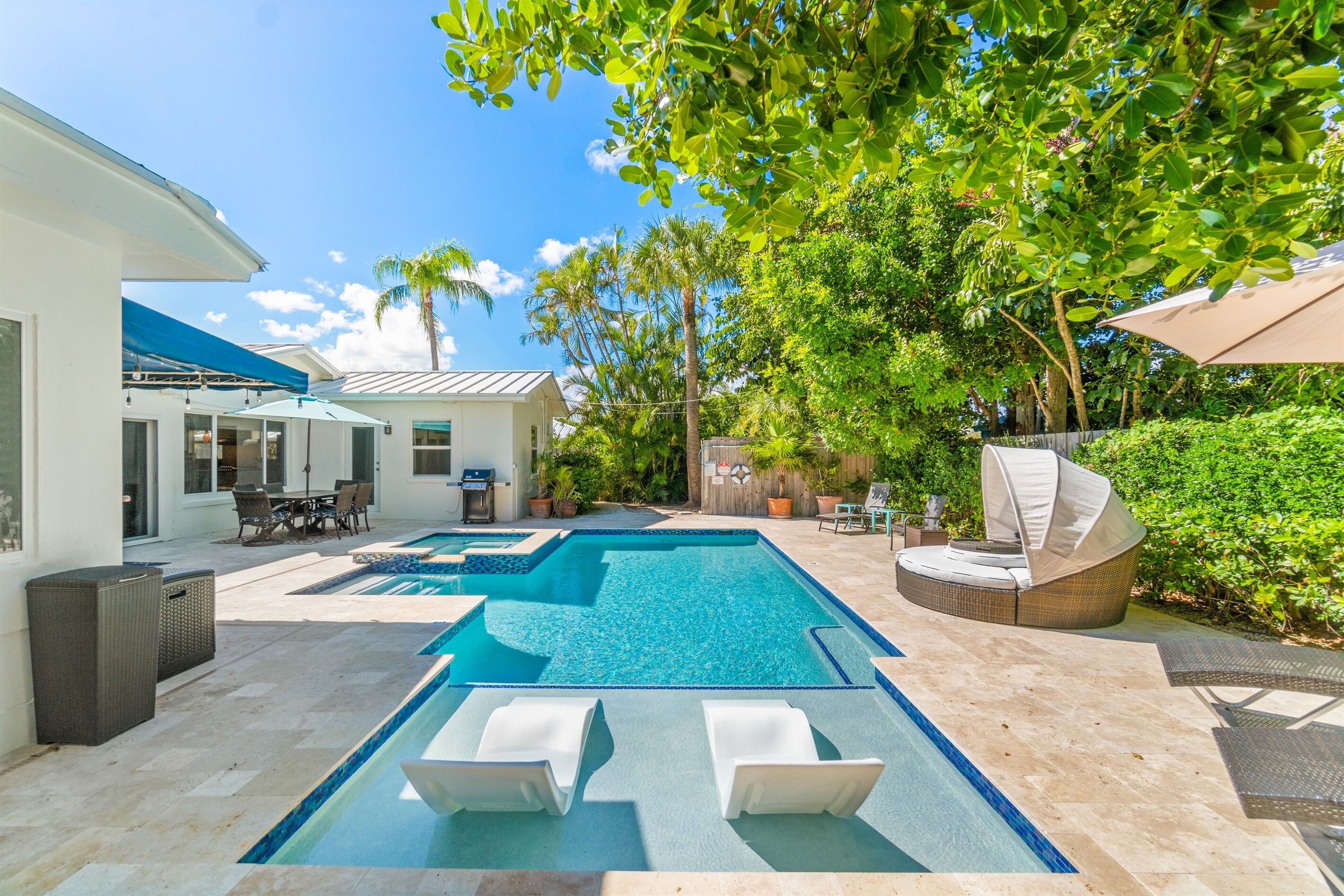 Une piscine avec des chaises longues, un patio couvert et une végétation luxuriante.