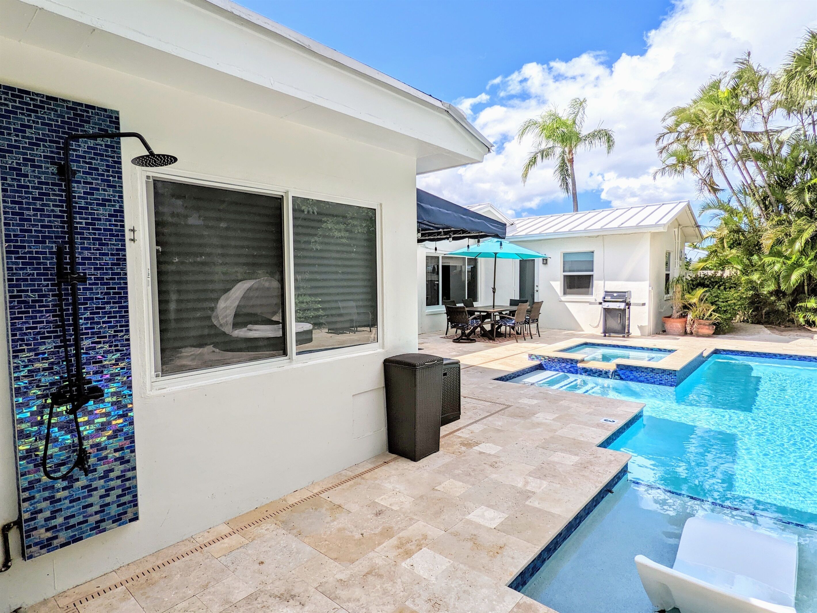 A residential backyard with a swimming pool, patio furniture, and a covered dining area.